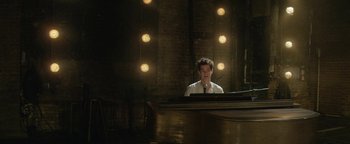Movie still from “tick, tick... BOOM!” (2021), directed by Lin-Manuel Miranda – A man sitting in front of a piano in front of lights; Medium shot, High angle