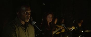 Movie still from “tick, tick... BOOM!” (2021), directed by Lin-Manuel Miranda – A group of people singing into microphones in the dark; Close Up shot, Over the shoulder angle