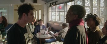 Movie still from “tick, tick... BOOM!” (2021), directed by Lin-Manuel Miranda – Two men are talking in a restaurant while other people sit in the background; Medium shot, Over the shoulder angle