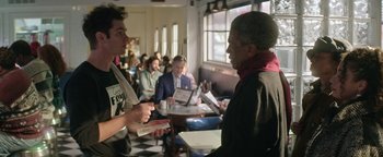 Movie still from “tick, tick... BOOM!” (2021), directed by Lin-Manuel Miranda – Two men are talking in a restaurant while other people are sitting in the background; Medium shot, Over the shoulder angle