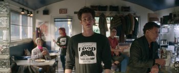 Movie still from “tick, tick... BOOM!” (2021), directed by Lin-Manuel Miranda – A young man wearing a t - shirt that says " good food " on it; Medium shot, Over the shoulder angle