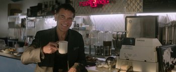 Movie still from “tick, tick... BOOM!” (2021), directed by Lin-Manuel Miranda – A man sitting at a table holding a mug; Medium shot, Over the shoulder angle