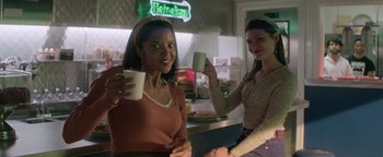Movie still from “tick, tick... BOOM!” (2021), directed by Lin-Manuel Miranda – Two women are holding cups of coffee in a bar; Medium shot, Low angle