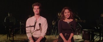 Movie still from “tick, tick... BOOM!” (2021), directed by Lin-Manuel Miranda – A man and a woman sitting next to each other on a stage with microphones; Medium shot, Low angle
