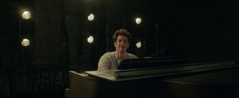 Movie still from “tick, tick... BOOM!” (2021), directed by Lin-Manuel Miranda – A man sitting in front of a piano in front of lights; Medium shot, Over the shoulder angle