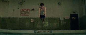 Movie still from “tick, tick... BOOM!” (2021), directed by Lin-Manuel Miranda – A man jumping into a swimming pool with a board; Wide shot, Overhead angle