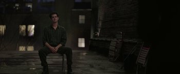 Movie still from “tick, tick... BOOM!” (2021), directed by Lin-Manuel Miranda – A man sitting on top of a bench in a dark room; Wide shot, High angle