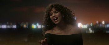 Movie still from “tick, tick... BOOM!” (2021), directed by Lin-Manuel Miranda – A woman with curly brown hair is singing; Medium shot, Over the shoulder angle