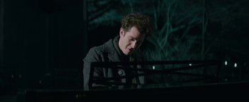 Movie still from “tick, tick... BOOM!” (2021), directed by Lin-Manuel Miranda – A man sitting in front of a piano in the dark; Medium shot, Over the shoulder angle