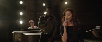 Movie still from “tick, tick... BOOM!” (2021), directed by Lin-Manuel Miranda – A man and a woman sing into microphones in front of another man; Medium shot, Over the shoulder angle