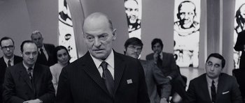 Movie still from “Solaris” (1972), directed by Andrei Tarkovsky – A man in a suit and tie standing next to two other men; Medium shot, Over the shoulder angle