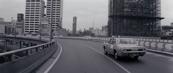 Movie still from “Solaris” (1972), directed by Andrei Tarkovsky – A car driving down a street next to tall buildings; Wide shot, Low angle