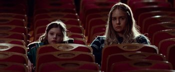 Movie still from “Steve Jobs” (2015), directed by Danny Boyle – Two young girls sitting in a row of seats; Close Up shot, Low angle