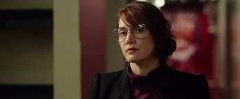 Movie still from “Steve Jobs” (2015), directed by Danny Boyle – A woman wearing glasses and a jacket looking to her left; Close Up shot, Over the shoulder angle