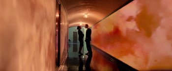 Movie still from “Steve Jobs” (2015), directed by Danny Boyle – A man and a woman standing next to each other in a hallway; Wide shot, Low angle