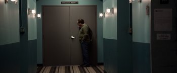 Movie still from “Steve Jobs” (2015), directed by Danny Boyle – A man leaning against a door in a room; Wide shot, Over the shoulder angle