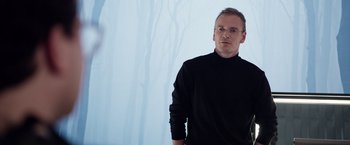 Movie still from “Steve Jobs” (2015), directed by Danny Boyle – A man wearing a black shirt and glasses; Medium shot, Over the shoulder angle