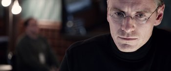 Movie still from “Steve Jobs” (2015), directed by Danny Boyle – A person wearing glasses and a black shirt; Close Up shot, Over the shoulder angle