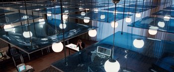 Movie still from “Steve Jobs” (2015), directed by Danny Boyle – A person sitting at a desk in a room with lights hanging from the ceiling; Wide shot, High angle