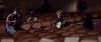 Movie still from “Steve Jobs” (2015), directed by Danny Boyle – A man sitting in an empty theater with his eyes closed; Wide shot, High angle