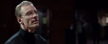 Movie still from “Steve Jobs” (2015), directed by Danny Boyle – An older man wearing glasses and a black shirt; Close Up shot, Over the shoulder angle