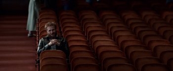 Movie still from “Steve Jobs” (2015), directed by Danny Boyle – A man sitting in a theater with rows of seats; Wide shot, High angle