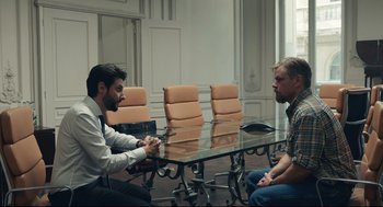 Movie still from “Stillwater” (2021), directed by Tom McCarthy – Two men sitting in front of each other at a conference table; Wide shot, Over the shoulder angle