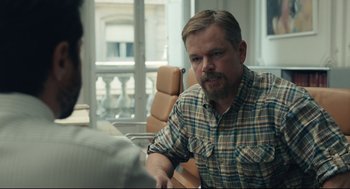 Movie still from “Stillwater” (2021), directed by Tom McCarthy – A man sitting at a table in front of a laptop computer; Medium shot, Over the shoulder angle