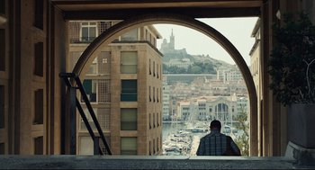 Movie still from “Stillwater” (2021), directed by Tom McCarthy – A man sitting on a ledge looking out over a city; Extreme Wide shot, Over the shoulder angle