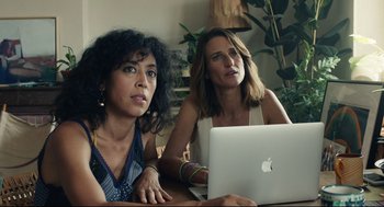 Movie still from “Stillwater” (2021), directed by Tom McCarthy – Two women sitting at a table with a laptop computer in front of them; Medium shot, Low angle