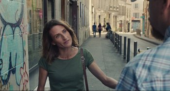 Movie still from “Stillwater” (2021), directed by Tom McCarthy – A woman is walking down the street with a purse; Medium shot, Over the shoulder angle