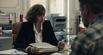 Movie still from “Stillwater” (2021), directed by Tom McCarthy – A woman sitting at a table with papers in her hands; Medium shot, Over the shoulder angle