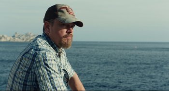 Movie still from “Stillwater” (2021), directed by Tom McCarthy – A man with a beard wearing a hat looking out at the ocean; Close Up shot, Over the shoulder angle