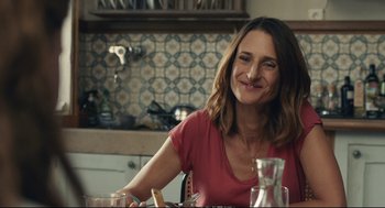 Movie still from “Stillwater” (2021), directed by Tom McCarthy – A woman sitting at a dining table smiling for the camera; Close Up shot, Over the shoulder angle