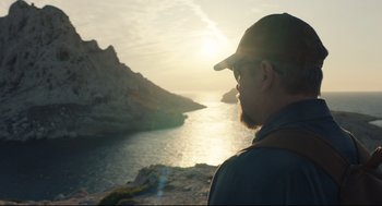 Movie still from “Stillwater” (2021), directed by Tom McCarthy – A man with a beard wearing a hat looking out at the water; Medium shot, Over the shoulder angle