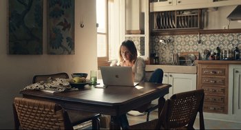 Movie still from “Stillwater” (2021), directed by Tom McCarthy – A woman sitting at a kitchen table looking at a computer; Medium shot, High angle