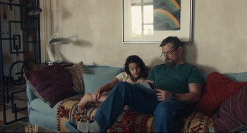 Movie still from “Stillwater” (2021), directed by Tom McCarthy – A man and a little girl sitting on a couch; Medium shot, Over the shoulder angle