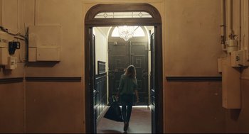 Movie still from “Stillwater” (2021), directed by Tom McCarthy – A woman walking through an open doorway with a bag; Wide shot, Low angle