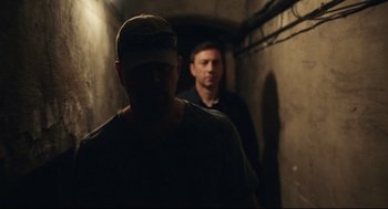 Movie still from “Stillwater” (2021), directed by Tom McCarthy – Two men are walking down a dark hallway; Medium shot, Over the shoulder angle