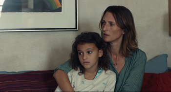 Movie still from “Stillwater” (2021), directed by Tom McCarthy – A woman sitting next to a young girl on a couch; Close Up shot, Over the shoulder angle