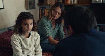 Movie still from “Stillwater” (2021), directed by Tom McCarthy – A woman and two children sitting on a couch; Medium shot, Over the shoulder angle