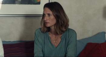 Movie still from “Stillwater” (2021), directed by Tom McCarthy – A woman sitting on a couch looking to her left; Close Up shot, Over the shoulder angle