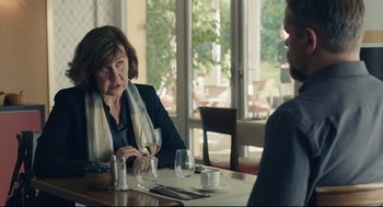 Movie still from “Stillwater” (2021), directed by Tom McCarthy – A woman sitting at a table in front of a glass of wine; Medium shot, Over the shoulder angle
