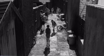 Movie still from “Belfast” (2021), directed by Kenneth Branagh – A black and white photo of a group of people walking down a street; Extreme Wide shot, High angle