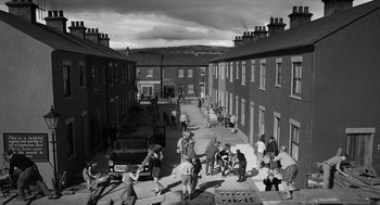 Movie still from “Belfast” (2021), directed by Kenneth Branagh – A black and white photo of a street with people walking on the sidewalk; Extreme Wide shot, High angle