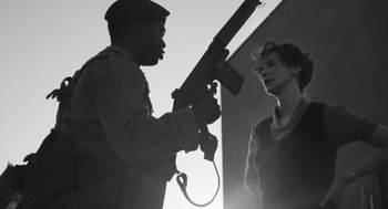 Movie still from “Belfast” (2021), directed by Kenneth Branagh – A black and white photo of a man and a woman holding a gun; Medium shot, Over the shoulder angle