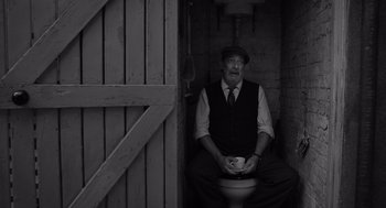 Movie still from “Belfast” (2021), directed by Kenneth Branagh – An older man sitting on a toilet in a room; Medium shot, Low angle