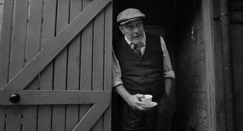 Movie still from “Belfast” (2021), directed by Kenneth Branagh – An old man holding a cup in his hand; Medium shot, Low angle