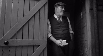 Movie still from “Belfast” (2021), directed by Kenneth Branagh – An older man holding a cup in his hand; Medium shot, Low angle