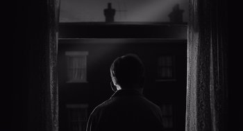 Movie still from “Belfast” (2021), directed by Kenneth Branagh – A man standing in front of a window in the dark; Medium shot, Low angle